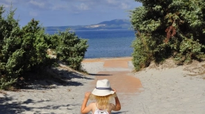 Kilkuletnia dziewczynka w białej sukience i kapeluszu idzie przez plażę w stronę morza