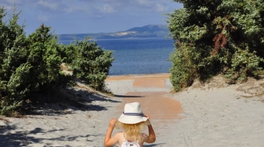 Kilkuletnia dziewczynka w białej sukience i kapeluszu idzie przez plażę w stronę morza